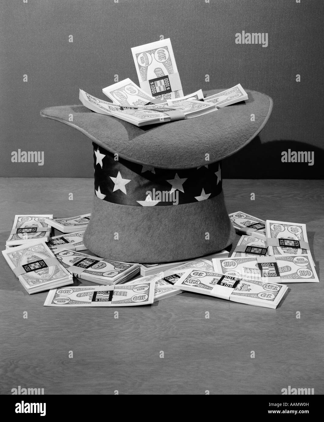 1940s SET-UP OF UPSIDE DOWN UNCLE SAM HAT FILLED WITH BUNDLES OF $100 BILLS OVERFLOWING AROUND IT Stock Photo