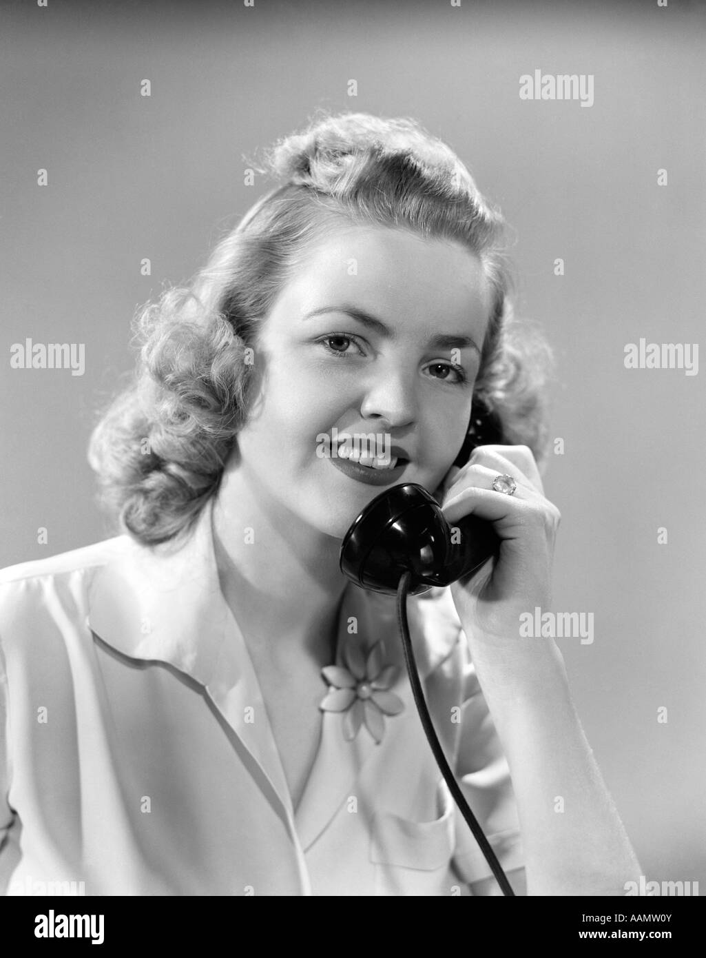 1940s YOUNG BLONDE WOMAN TALKING ON TELEPHONE LOOKING AT CAMERA Stock Photo