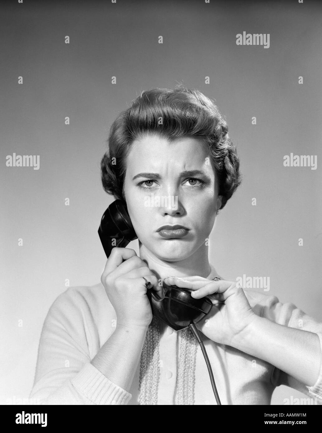 1950s WOMAN HOLDING RECEIVER HAND OVER RECEIVER LOOKING AT CAMERA WITH ANNOYED ANGRY EXPRESSION Stock Photo