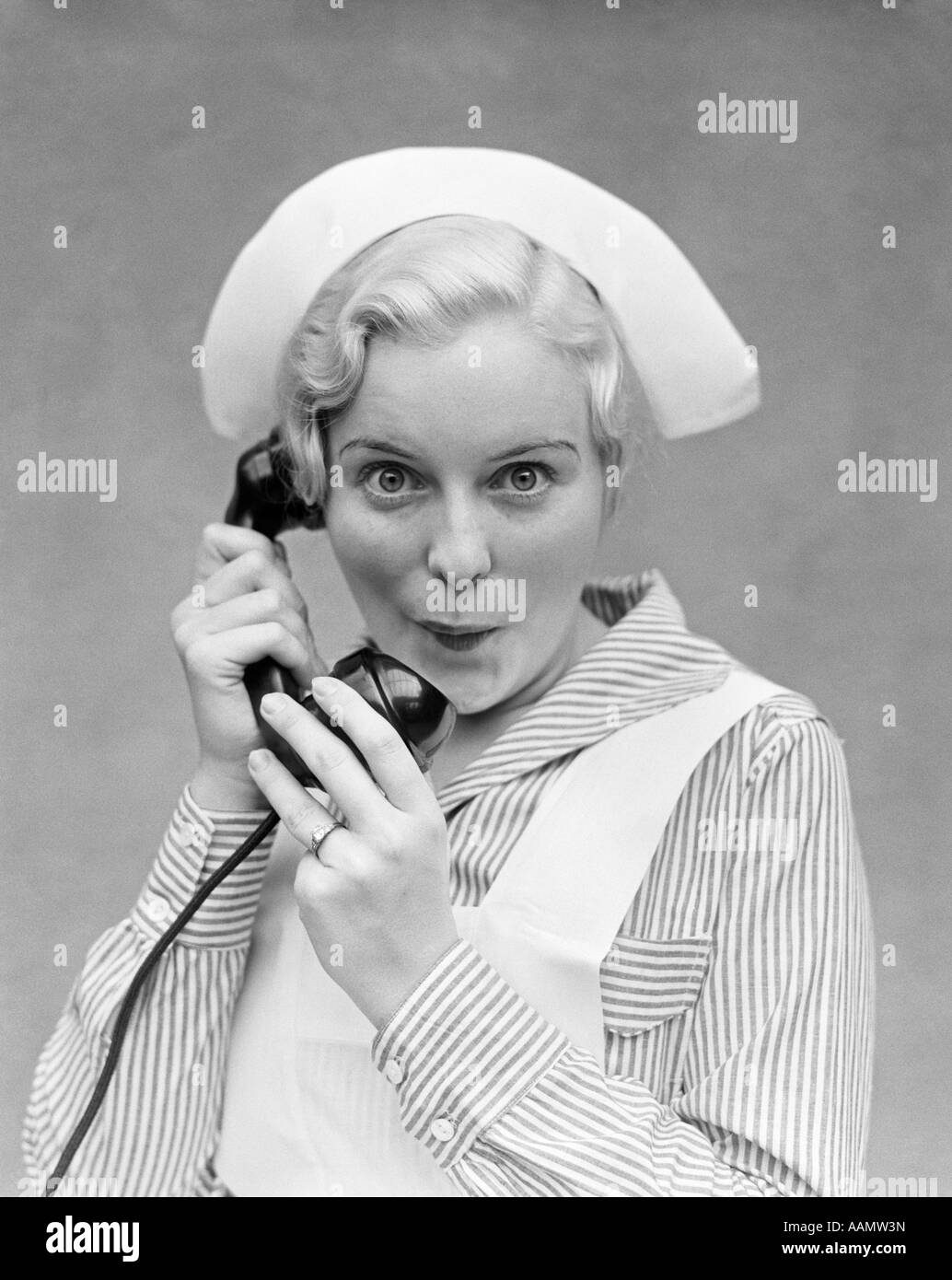 1920s 1930s BLONDE NURSE TALKING ON TELEPHONE LOOKING AT CAMERA WITH FUNNY FACIAL EXPRESSION Stock Photo