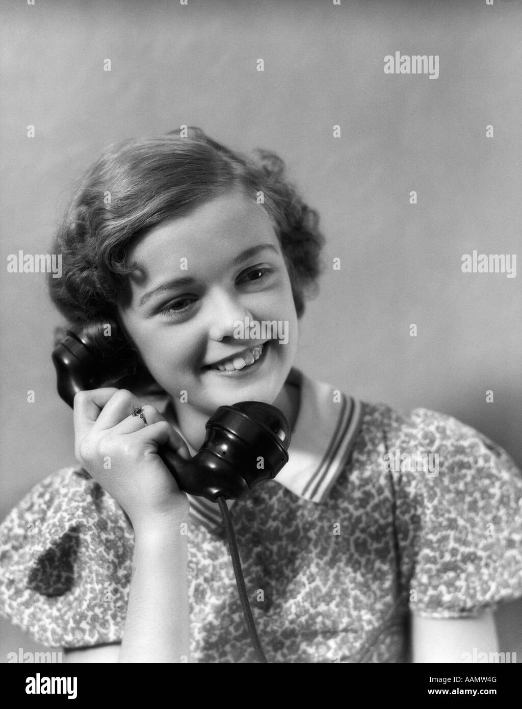 1930s TEEN GIRL SMILING BRUNETTE PRINT DRESS TALKING ON TELEPHONE Stock Photo