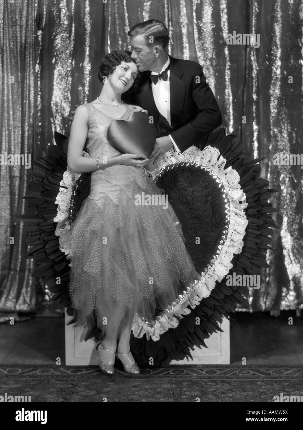 1920s COUPLE PORTRAIT MAN KISSING WOMAN HOLDING SATIN VALENTINE HEART Stock Photo