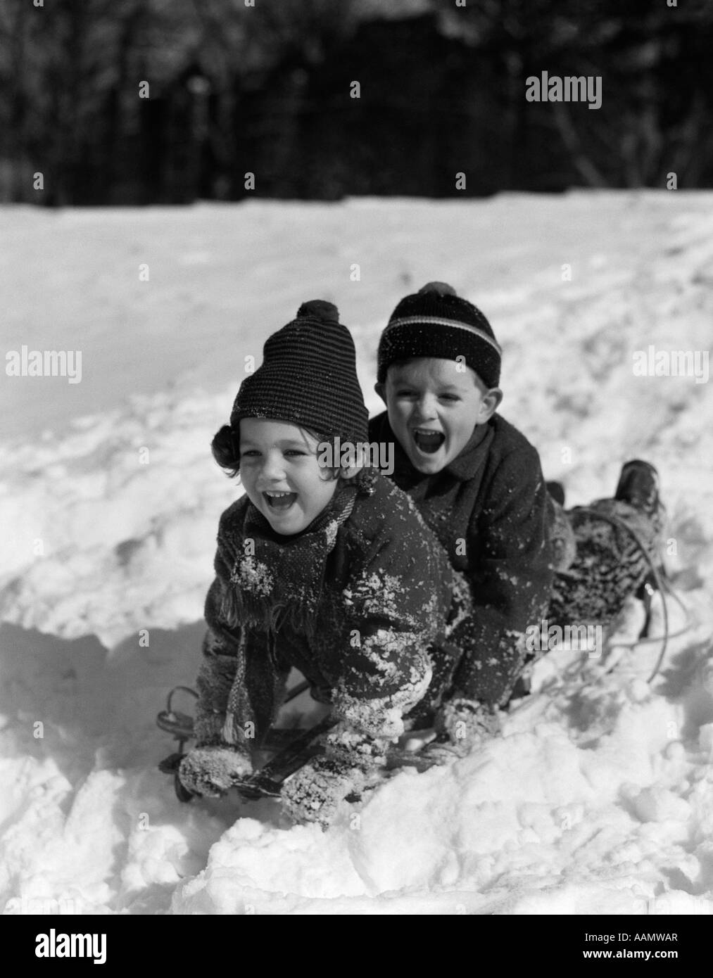 1930s BOY AND GIRL LAUGHING SLEDDING IN SNOW Stock Photo