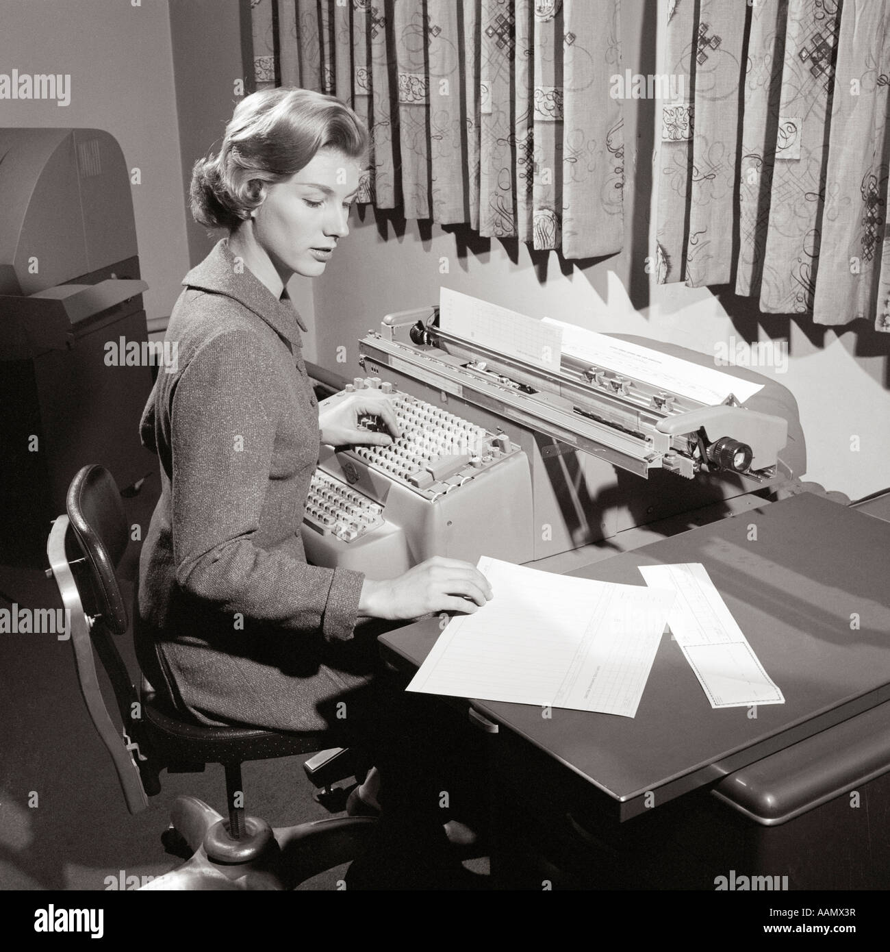 1950s SECRETARY SITTING AT DESK READING ...