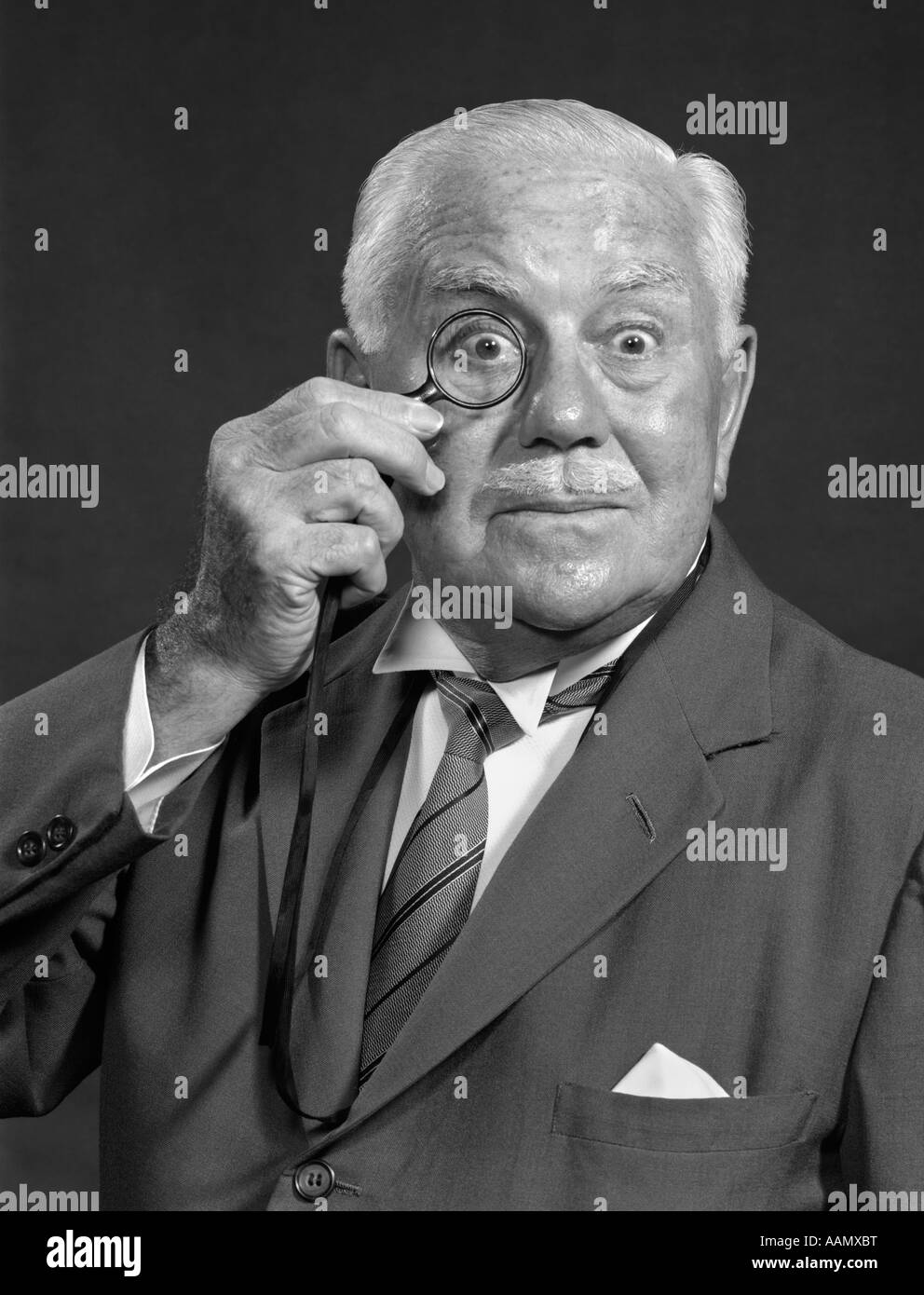 1950s CHARACTER PORTRAIT ELDERLY MAN TIE FORMAL JACKET HOLDING MONOCLE SURPRISED FUNNY FACIAL EXPRESSION Stock Photo