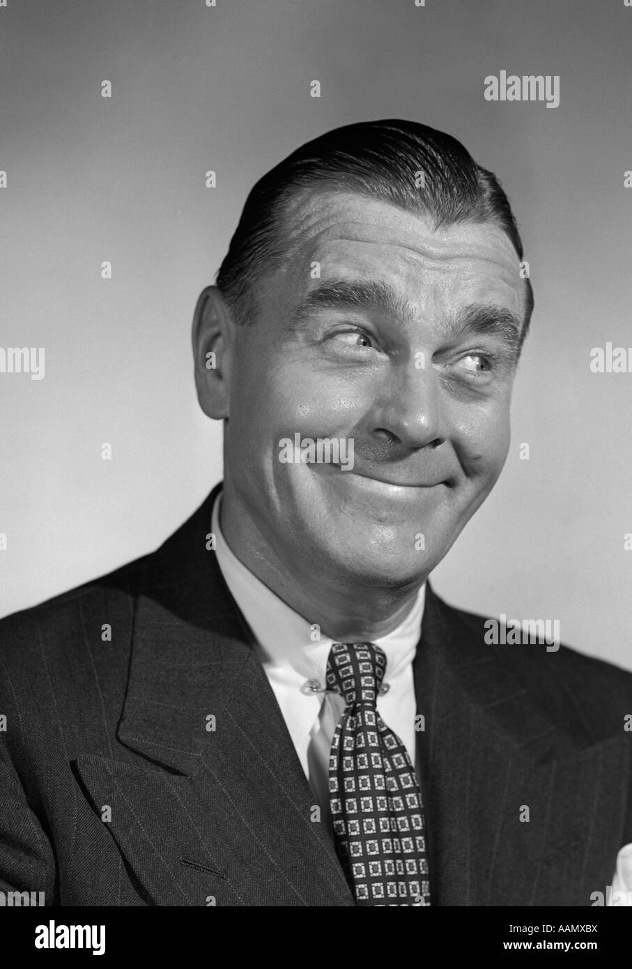 1950s MAN SMILING BUSINESSMAN WITH FUNNY AMUSED FACIAL EXPRESSION LOOKING OFF TO SIDE AWAY Stock Photo