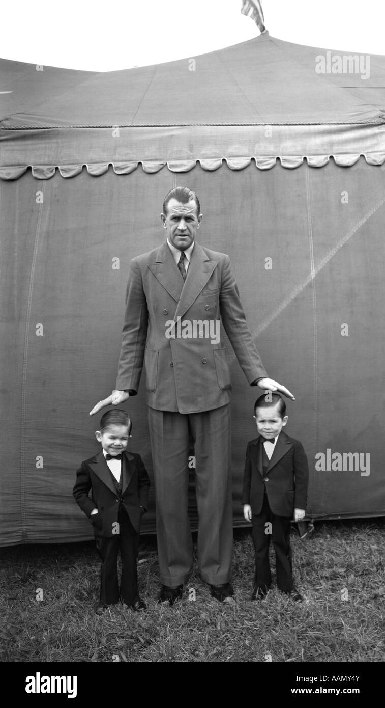 1930s 1939 EXTREMES DANBURY FAIR BROTHERS JACK AND BILL TWO SMALLEST MEN IN WORLD STANDING NEXT TO TALL MAN Stock Photo