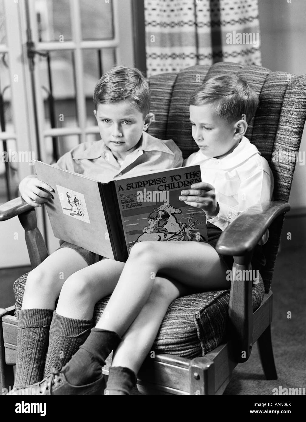 1940s TWO BOYS SITTING IN ONE CHAIR SHARING LARGE BOOK ARMCHAIR Stock Photo