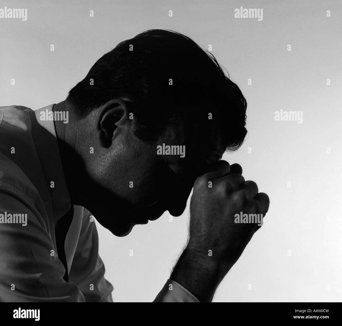 1950s SILHOUETTED MAN HEAD DOWN HAND TO FOREHEAD PRAYING PRAYER DEPRESSED DEPRESSION SAD WORRIED Stock Photo