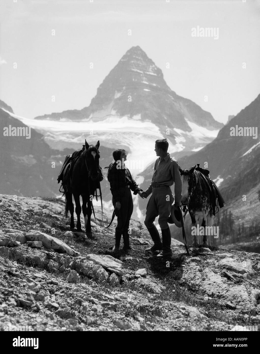 1930s COUPLE MAN WOMAN HOLDING HANDS STANDING WITH HORSES IN MOUNTAINS WESTERN MT. ASSINIBOINE CANADA Stock Photo