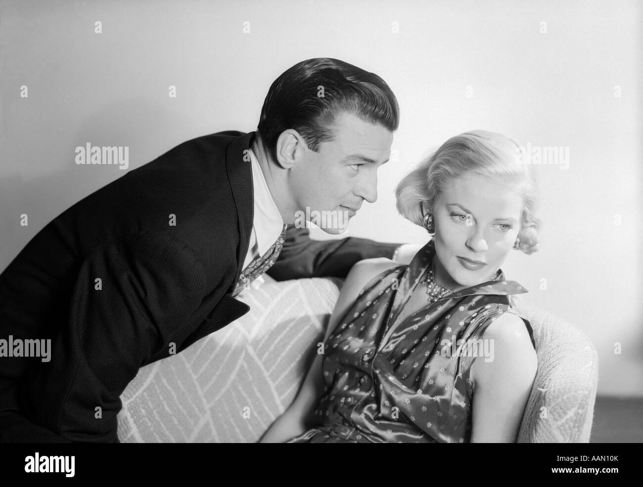 1950s COUPLE WITH THE WOMAN SITTING LOOKING AWAY MAN PROFILE LOOKING BLOND HAIR WELL DRESSED SATIN Stock Photo