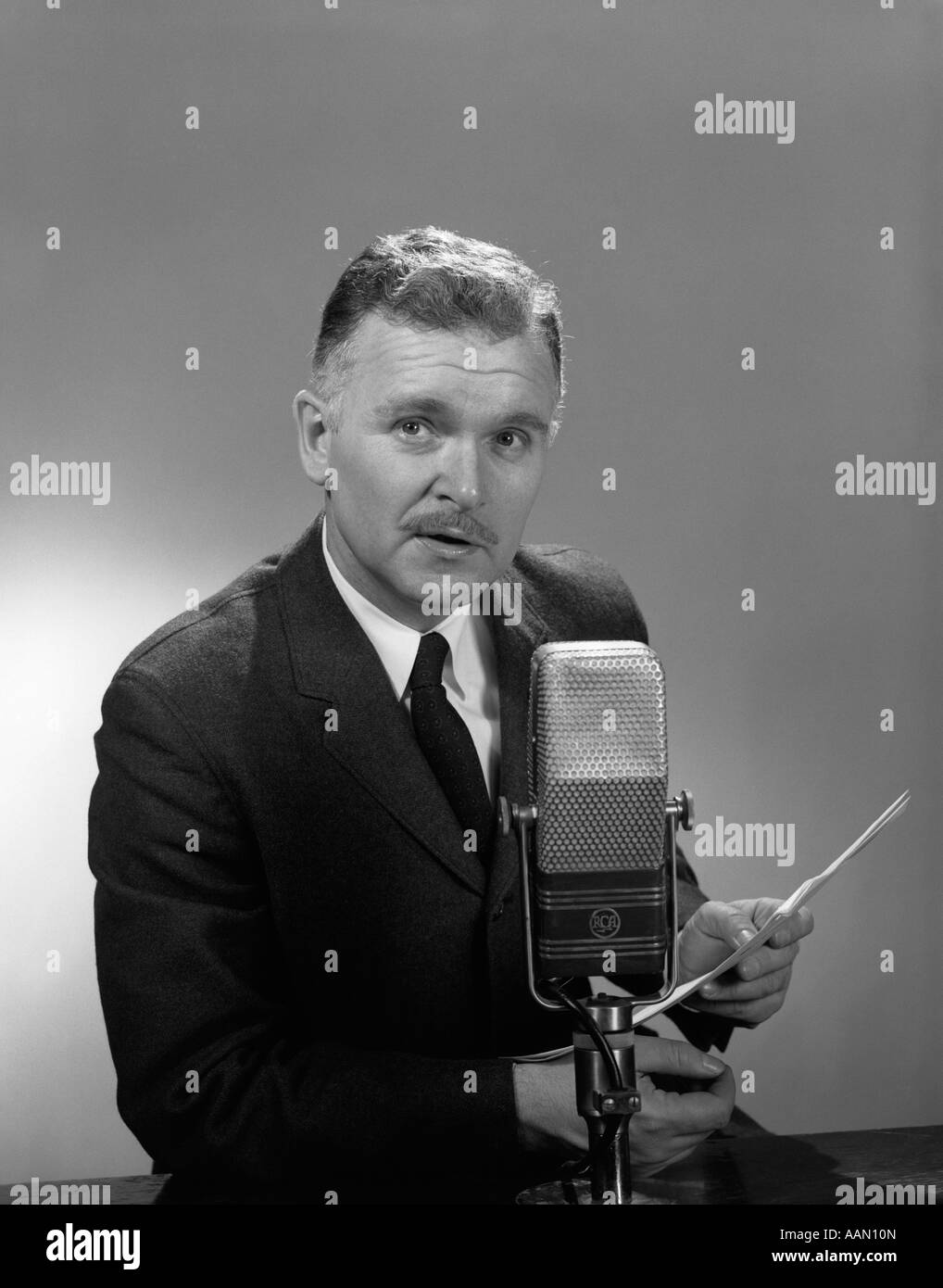 1950s 1960s OLDER MAN SPEAKING INTO MICROPHONE HOLDING PAPERS RADIO TELEVISION NEWSMAN REPORTER ANNOUNCER Stock Photo