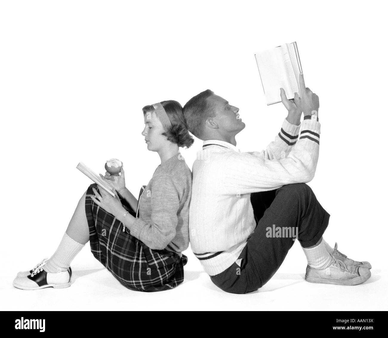 1950s 1960s TEENAGE HIGH SCHOOL COUPLE BOY & GIRL STUDENTS LEANING BACK TO BACK DATING STUDYING READING BOOKS Stock Photo