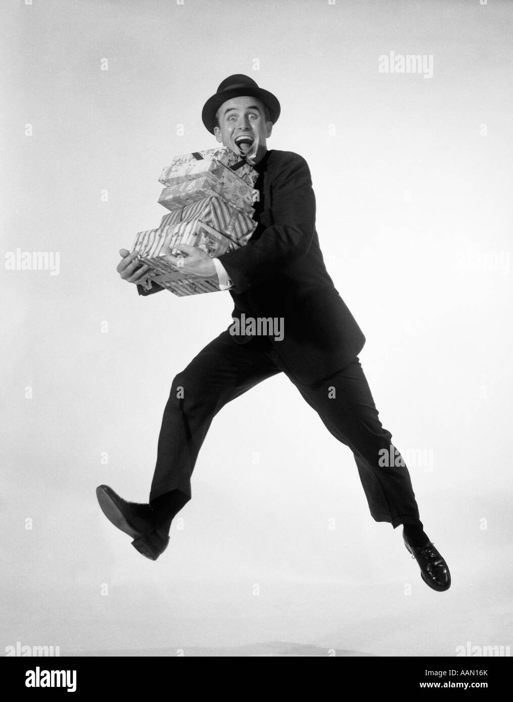 1960s EXCITED ENTHUSIASTIC MAN JUMPING IN AIR RUNNING CARRYING PILE PRESENTS GIFTS PACKAGES Stock Photo