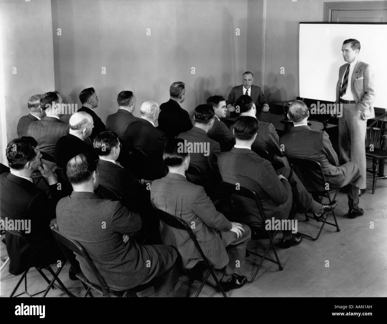 1940s EXECUTIVES IN ROWS OF FOLDING CHAIRS AT MEETING WITH CHAIRMAN IN FRONT OF ROOM BANGING GAVEL ON TABLE Stock Photo
