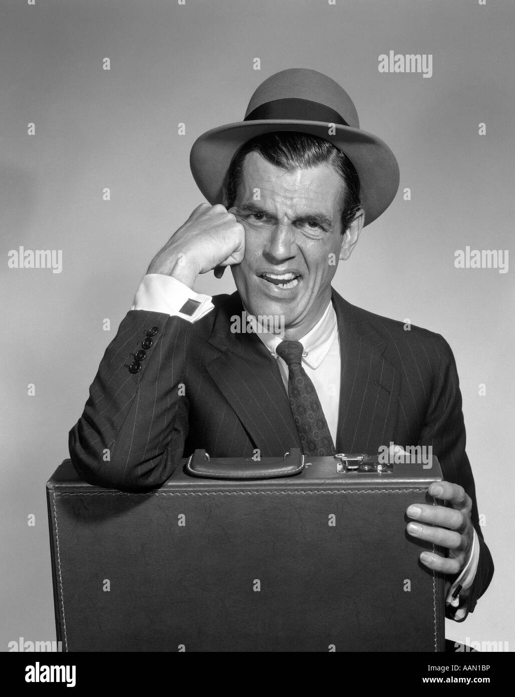 1960s DISGUSTED MAN WITH SCOWL ON FACE WEARING HAT SHIRT TIE SUIT ONE ELBOW RESTING ON BRIEFCASE ANGRY UPSET Stock Photo