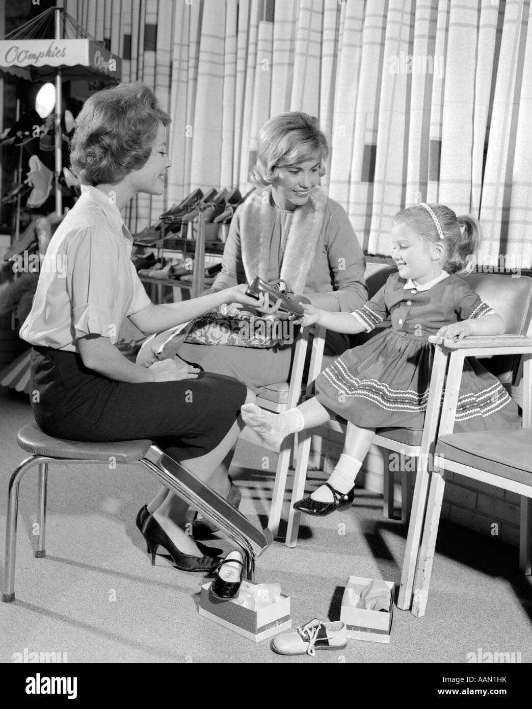 1960s MOTHER DAUGHTER SHOE SHOPPING SALESWOMAN SHOWING PATENT LEATHER SHOE TO GIRL IN RETAIL STORE Stock Photo