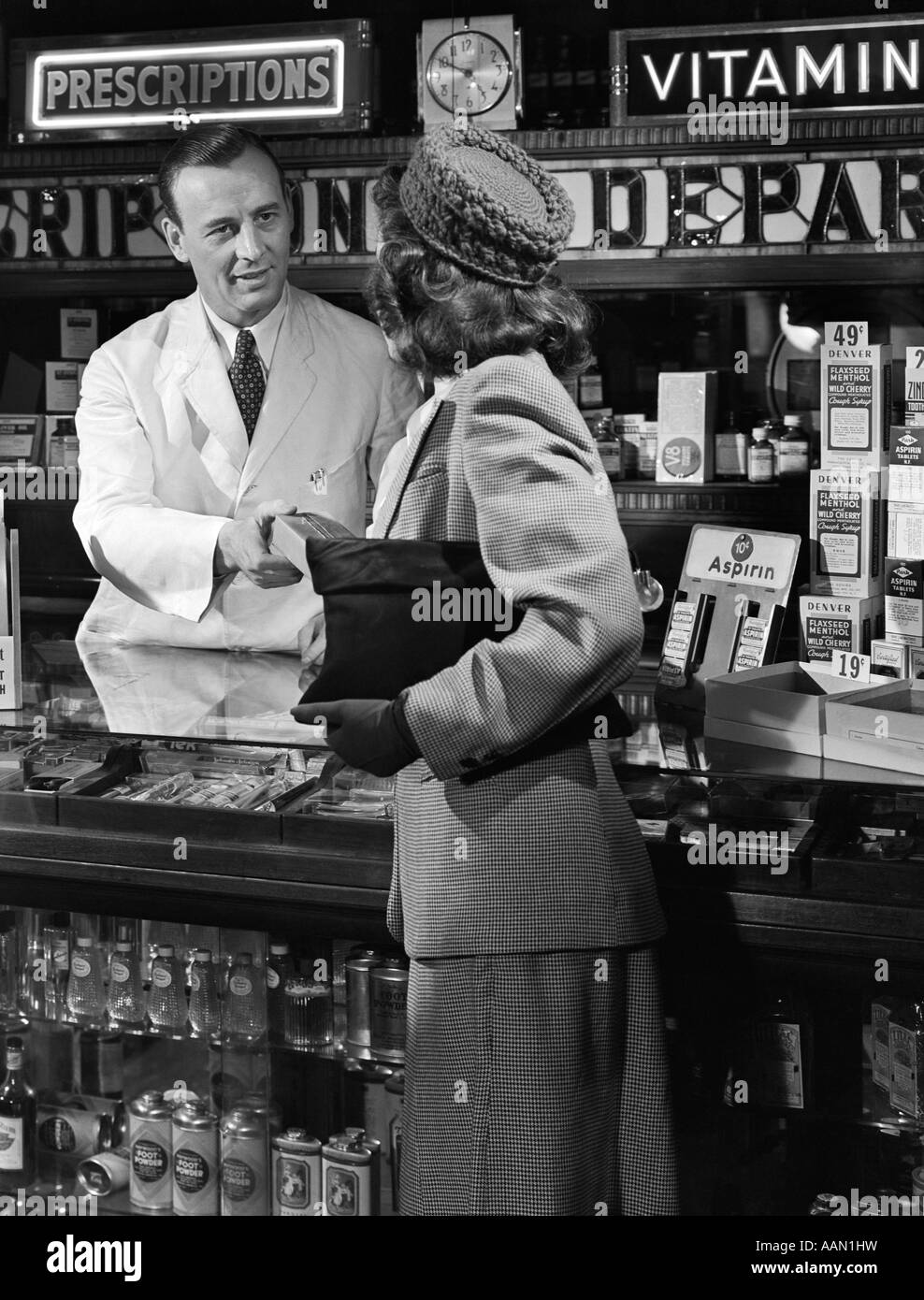 1940s 1950s WOMAN FROM BEHIND ACCEPTING BOX FROM MAN PHARMACIST AT DRUG COUNTER PHARMACY Stock Photo