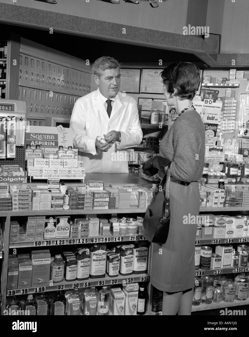 1960s WOMAN COUNTER PHARMACY TALK TALKING PHARMACIST BUYING DRUGS PRODUCT CUSTOMER SALES SERVICE RETRO DRUG STORE Stock Photo