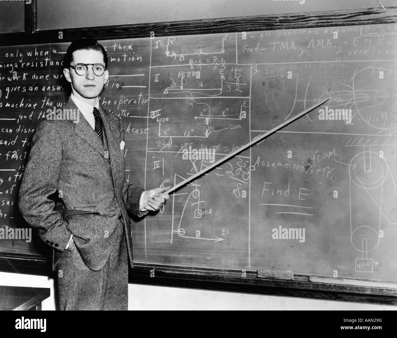 1930s 1940s MAN TEACHER PROFESSOR POINTING POINTER AT BLACKBOARD LOOKING AT CAMERA Stock Photo