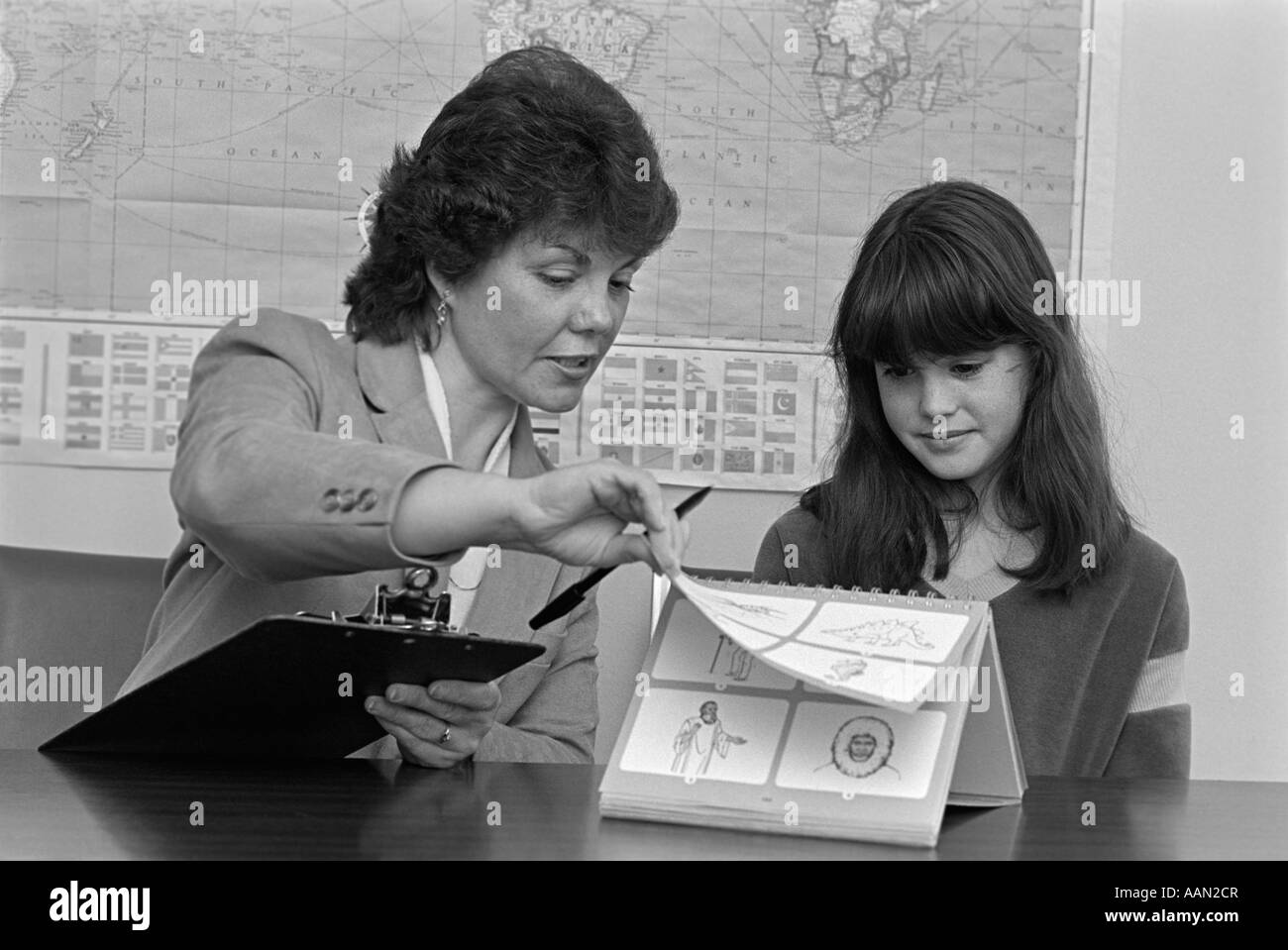 1980s GRADE SCHOOL TEACHER HOLDING CLIPBOARD TESTING FEMALE STUDENT Stock Photo