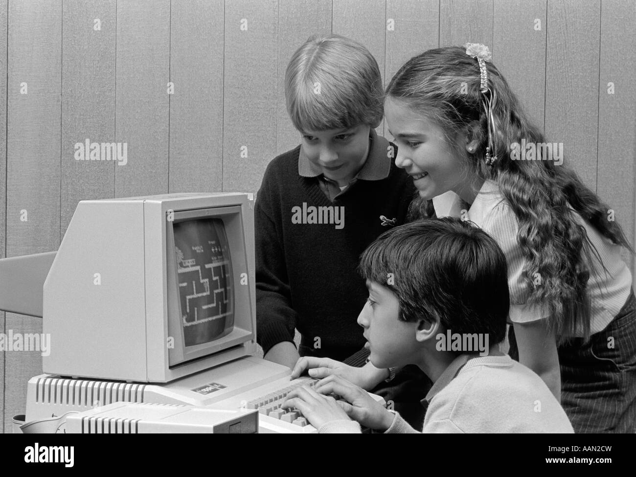 1980s BOY SITTING IN FRONT OF COMPUTER PLAYING GAMES BOY & GIRL LOOKING ON OVER HIS SHOULDER Stock Photo