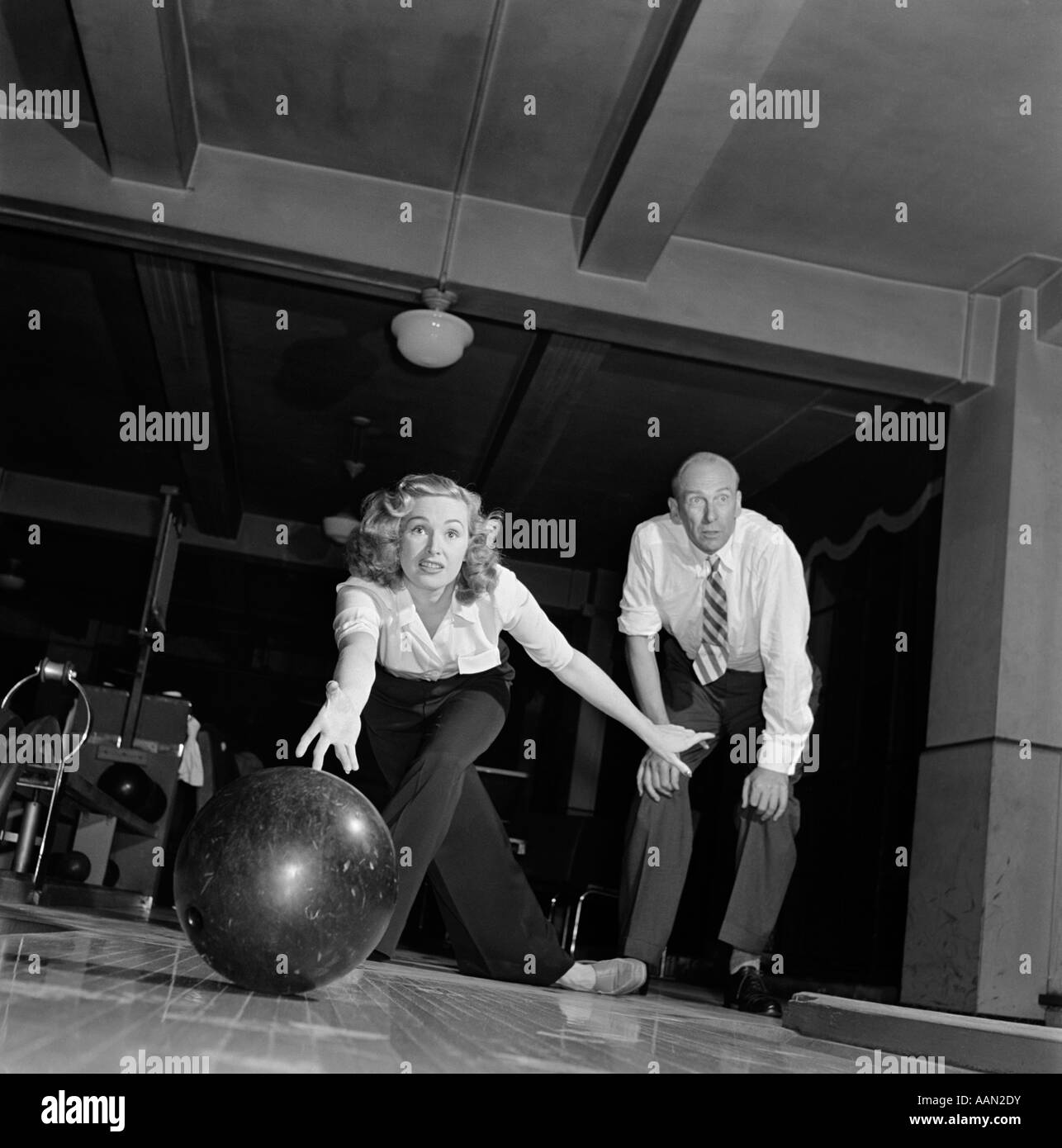 1950s WOMAN RELEASING BOWLING BALL DOWN ALLEY MAN WATCHING Stock Photo