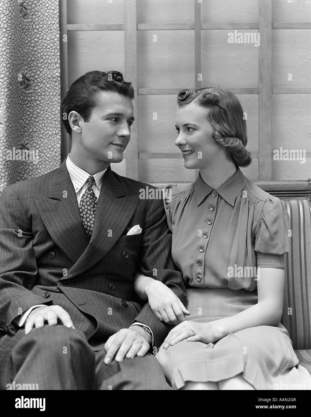 1930s 1940s COUPLE SITTING IN CHAIR ARMS LOCKED LOOKING AT ONE ANOTHER Stock Photo