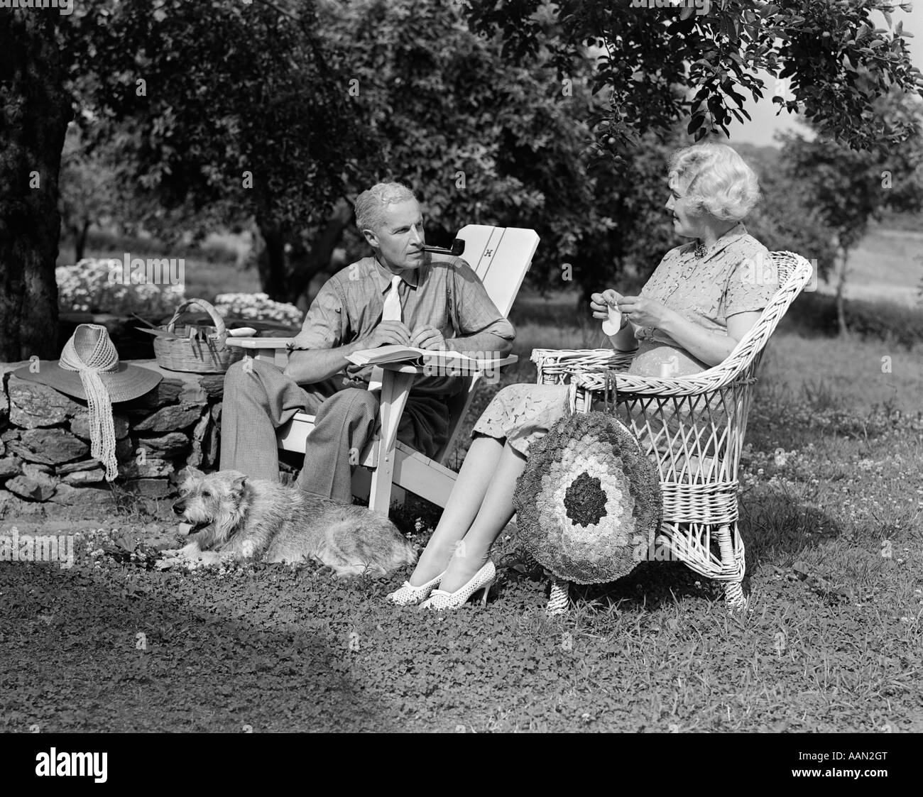1930s 1940s Senior Retired Couple Sitting Outdoor Lawn Chairs Man Smoking Pipe Woman Knitting