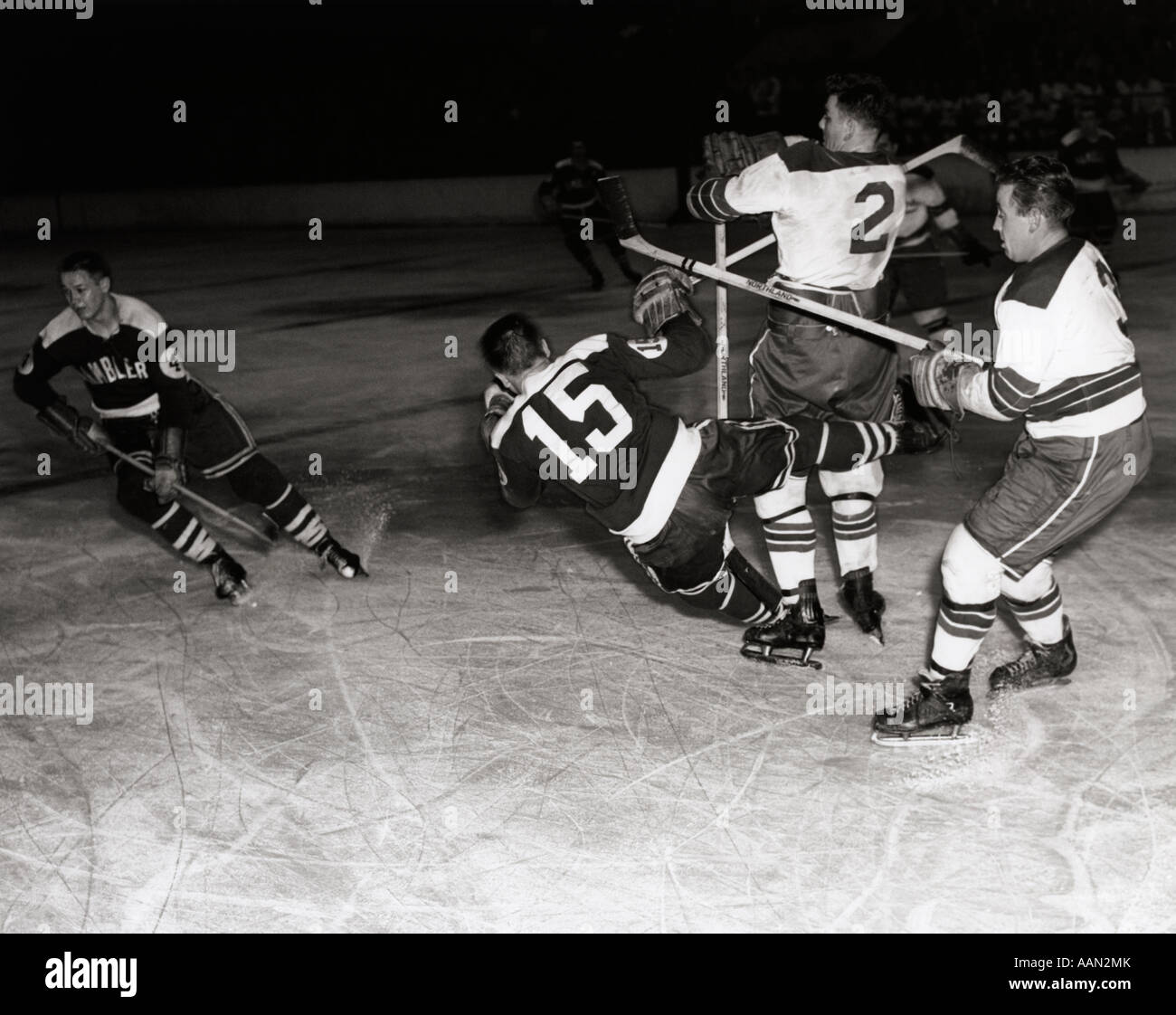 1950s HOCKEY GAME WITH ONE OF 4 PLAYERS IN FOREGROUND BEING KNOCKED DOWN BY 2 OPPOSING TEAM MEMBERS Stock Photo