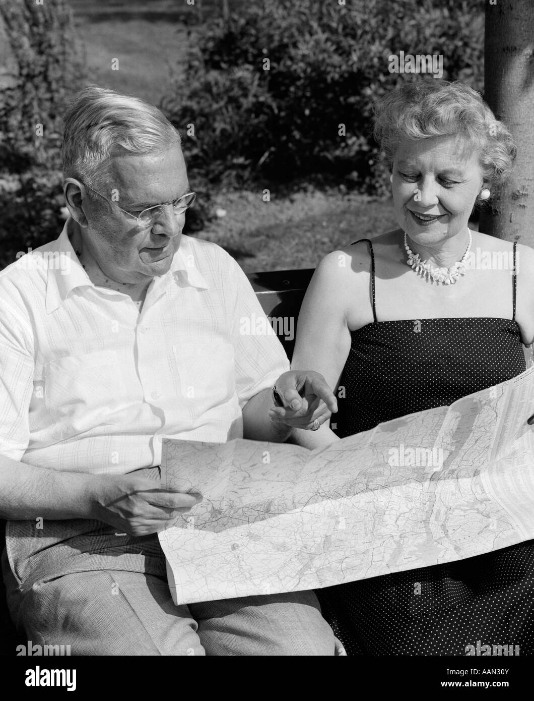 1950s ELDERLY COUPLE SEATED ON BENCH LOOKING AT MAP Stock Photo