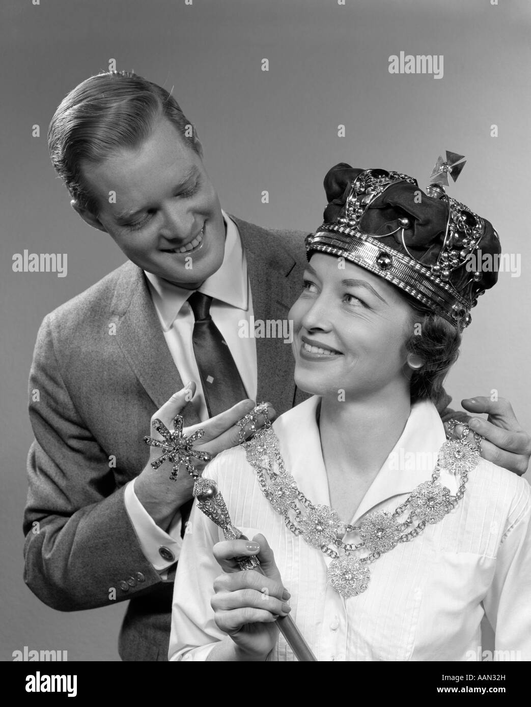 1950s MAN HOLDING ROYAL NECKLACE ON WOMAN WEARING CROWN AND HOLDING SCEPTER Stock Photo