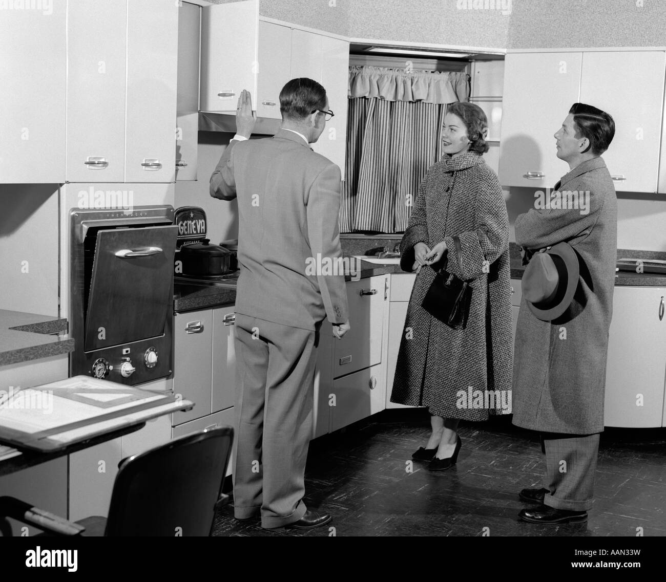 1950s SALESMAN IN MODEL KITCHEN WITH COUPLE Stock Photo