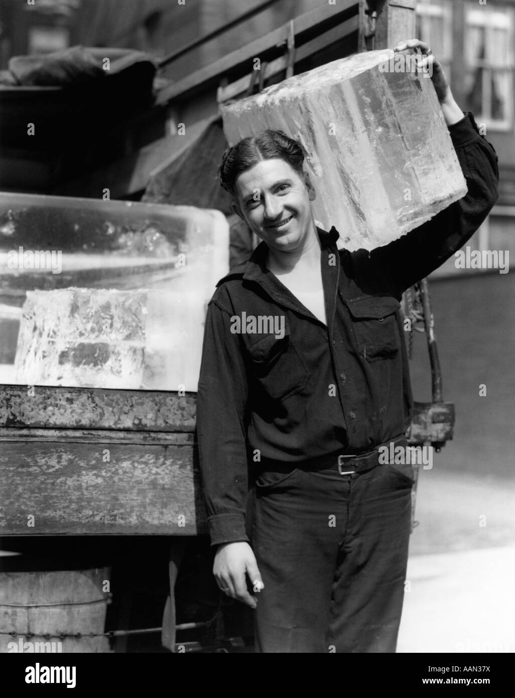 1930s ice delivery man carrying large block of ice on shoulder looking