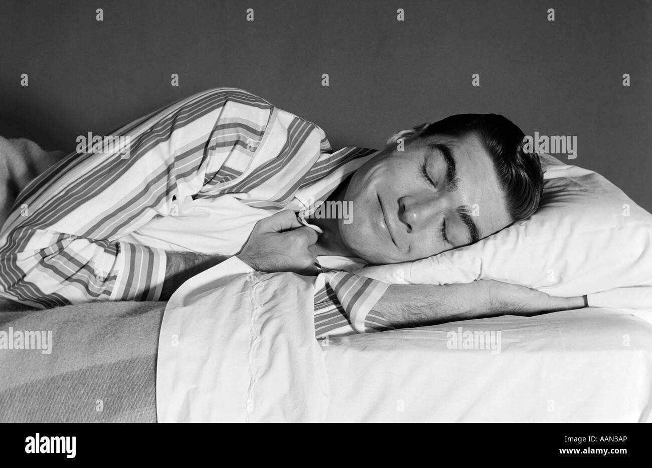 1950s 1960s MAN IN STRIPED PAJAMAS SMILING ASLEEP IN BED Stock Photo