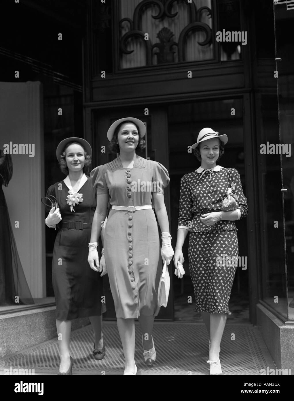 1930s THREE SMILING FASHIONABLE DRESSED WOMEN SHOPPING WALKING FROM RETAIL DEPARTMENT STORE Stock Photo