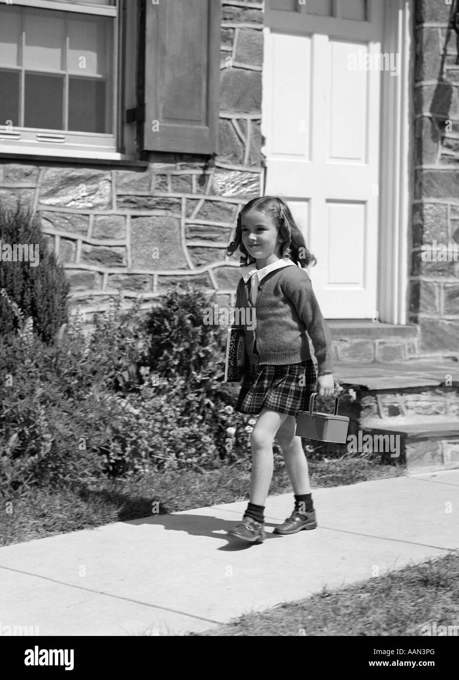 1940s LITTLE GIRL WALKING TO SCHOOL OUTSIDE OF HOME DOORWAY CARRYING LUNCH BOX Stock Photo