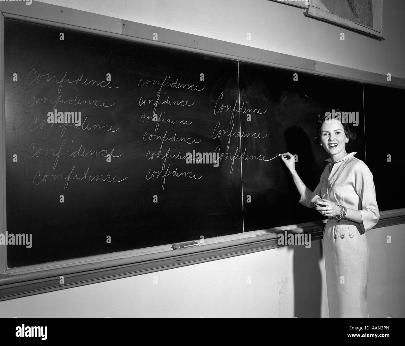1950s TEACHER IN FRONT OF CLASSROOM WRITING CONFIDENCE ON BLACKBOARD Stock Photo