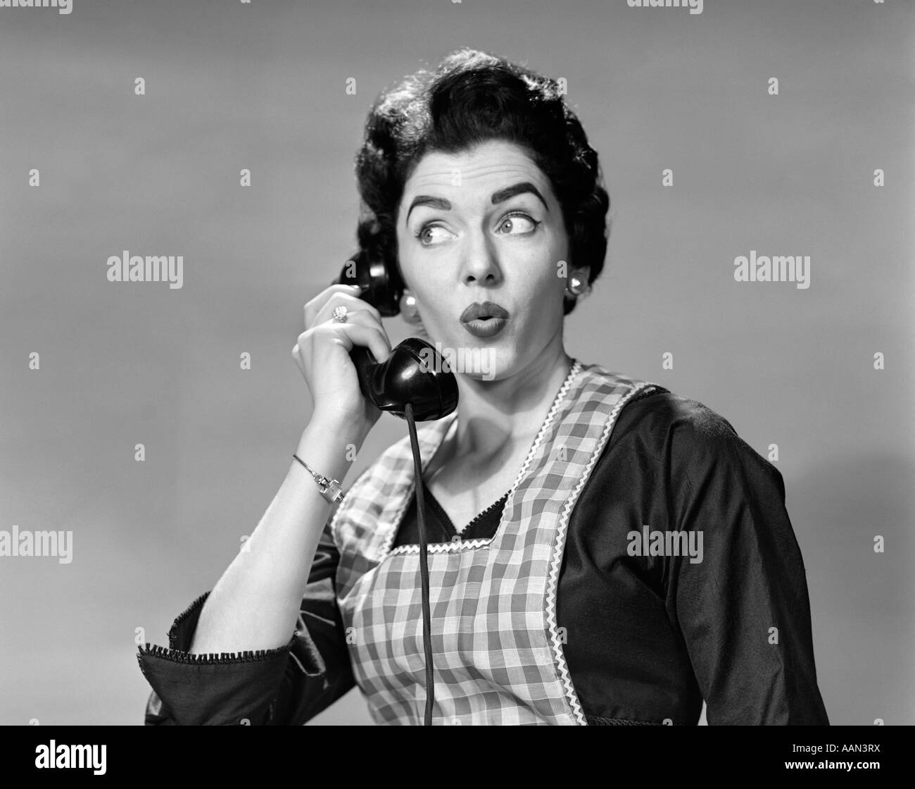 1950s WOMAN WEARING APRON TALKING ON TELEPHONE WITH EXAGGERATED SURPRISED EXPRESSION Stock Photo
