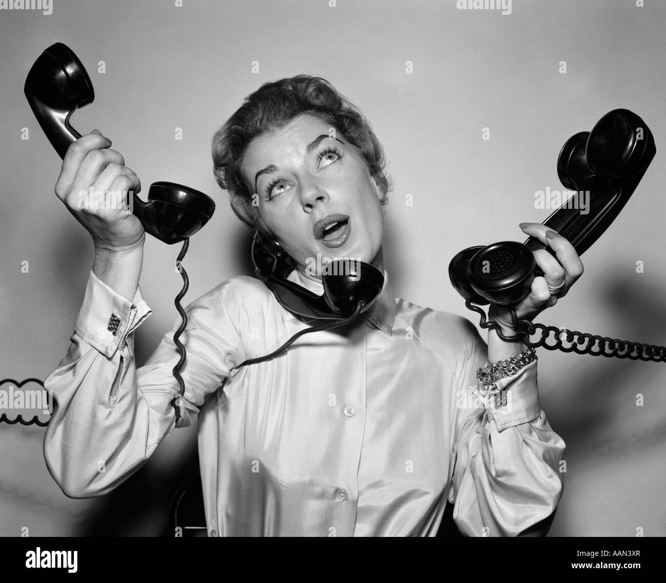 1950s HARRIED WOMAN HOLDING FOUR TELEPHONES TALKING ON ONE Stock Photo