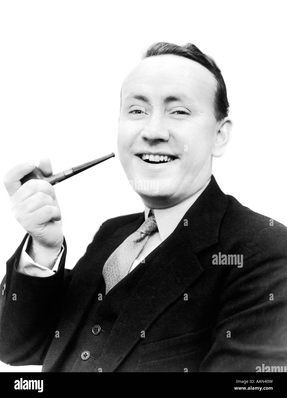 1940s 1930s MAN HOLDING PIPE IN HIS HAND SMILING LOOKING AT CAMERA DRESSED IN SUIT AND TIE SMOKING TOBACCO Stock Photo