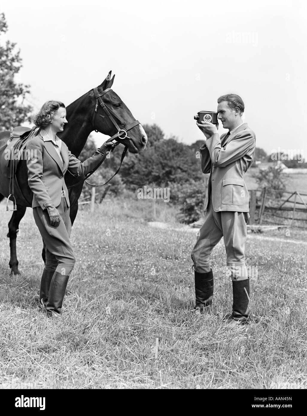 1940s SMILING EQUESTRIAN COUPLE THE WOMAN IS HOLDING THE HORSE BRIDLE WHILE THE MAN IS TAKING HOME MOVIE Stock Photo