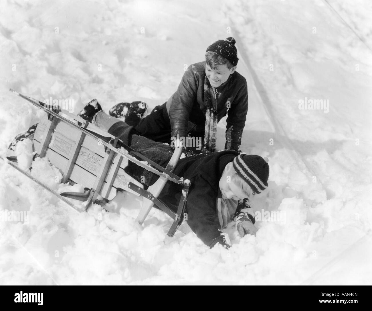 1930s 1940s TWO BOYS LAUGHING IN SNOW FALLING OFF OF SLED THAT IS TURNED ON ITS SIDE Stock Photo