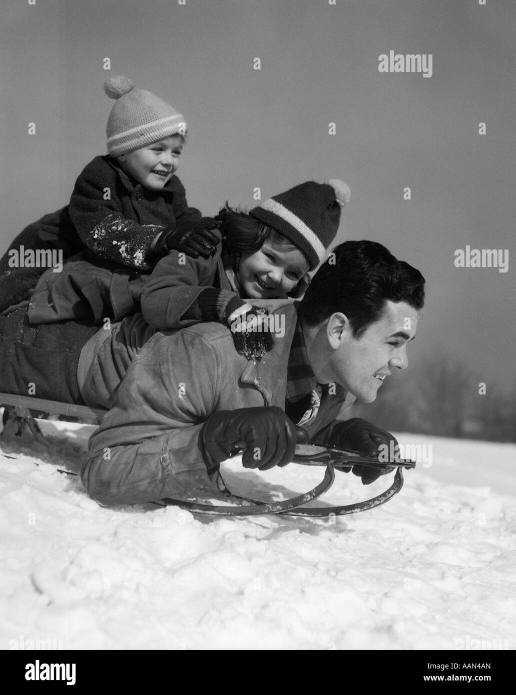 1930s FATHER DAUGHTER AND SON PILED ON SLED GOING DOWNHILL IN SNOW LAUGHING Stock Photo