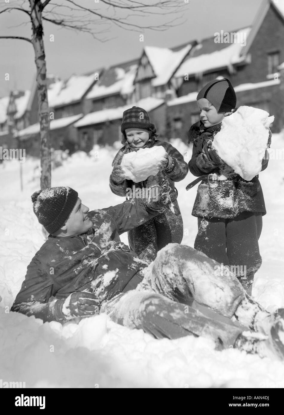 1930s 1940s MAN FATHER TWO CHILDREN PLAYING IN WINTER SNOW Stock Photo
