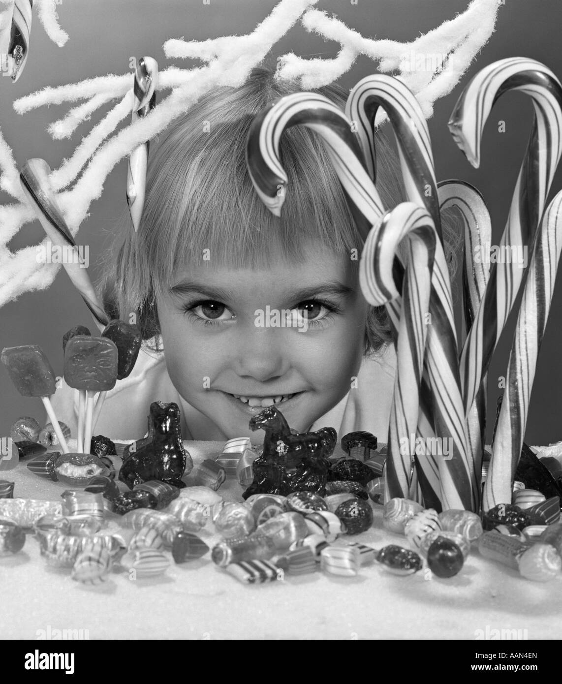 1950s 196s SMILING LITTLE BLOND GIRL PEEKING IN WINDOW CANDY STORE DISPLAY EYES WIDE LOOKING AT CAMERA Stock Photo
