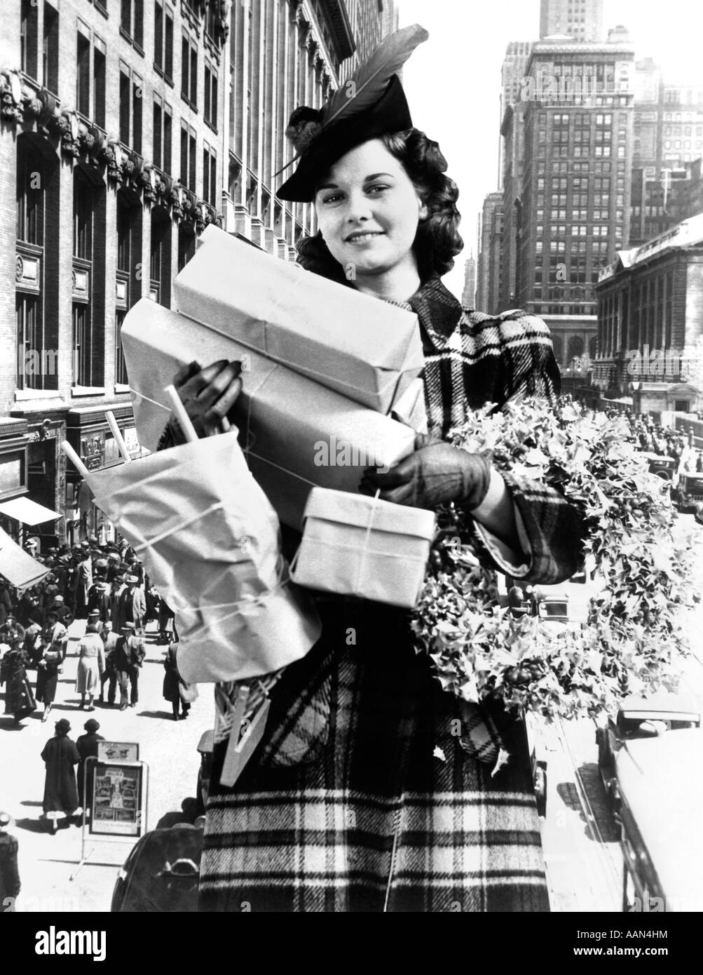 1930s 1940s WOMAN LOOKING AT CAMERA ARMS FULL WITH CHRISTMAS SHOPPING PACKAGES & WREATH COMPOSITE WITH STREET SCENE Stock Photo