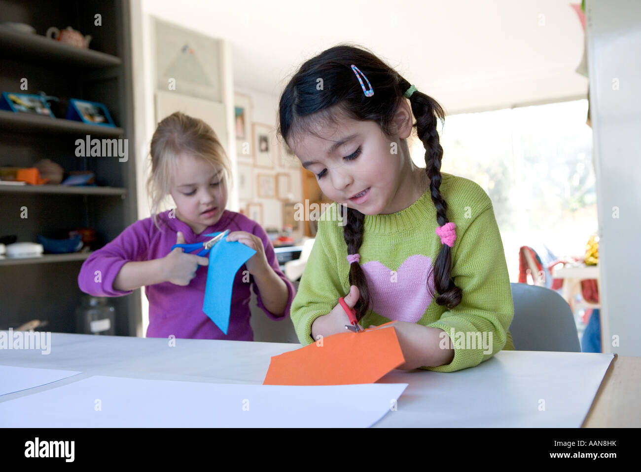 Two little girls are cutting coloured paper with scissors Stock Photo