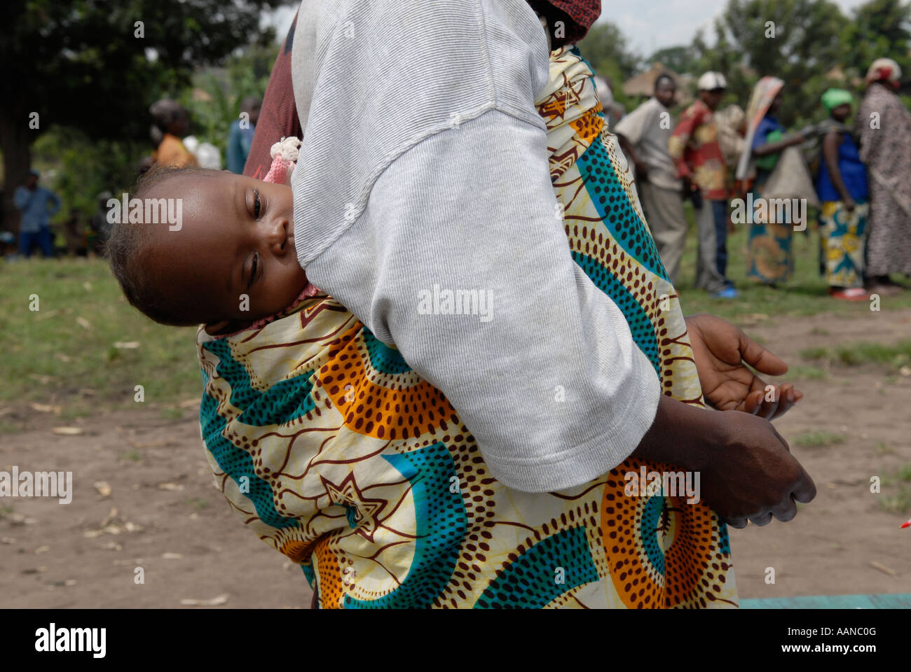 A woman carries a baby on her back as she waits for food distribution carried out by the World Food Program WFP in North Kivu province DR Congo Stock Photo