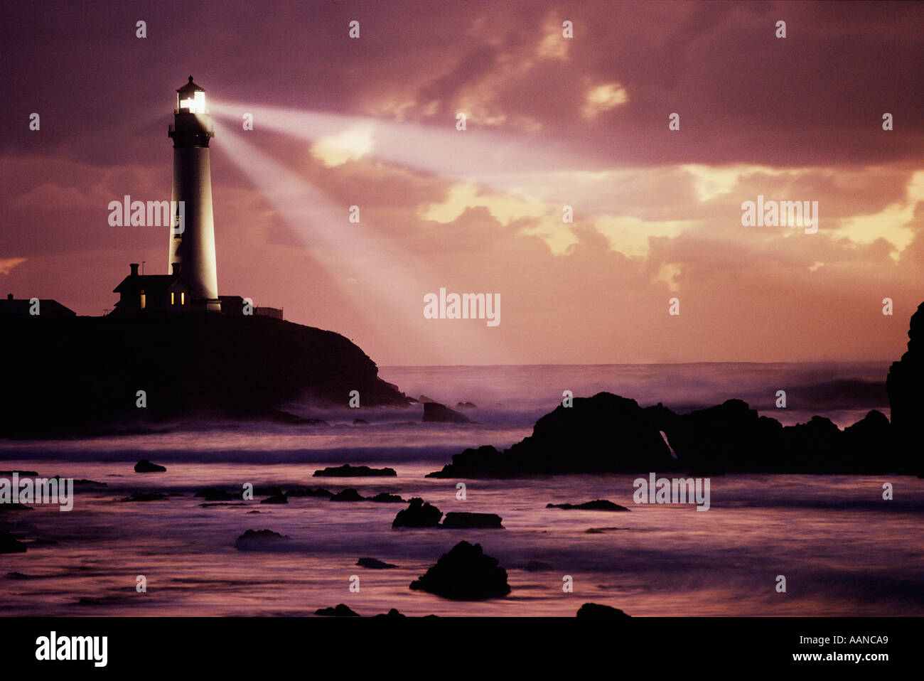 Pigeon Point Lighthouse casting beam across rocky shore and sunset skies. Image is not digitally altered - No photo shop.  REAL! Stock Photo